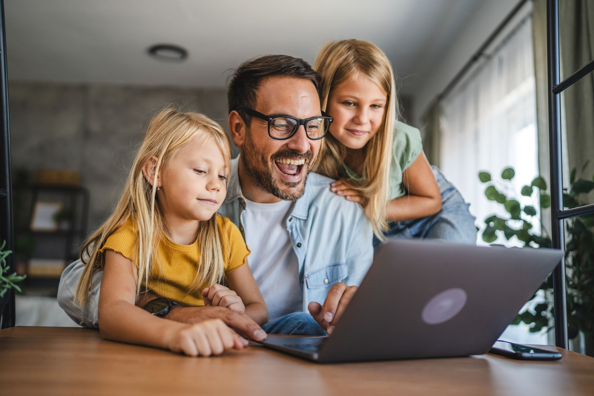 Father and daughters smile and use laptop at home together happy